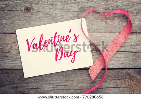 Blank valentines greeting card and red heart shaped ribbon on wooden background