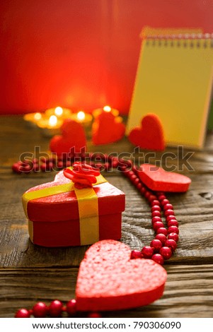 Gift box in the shape of a heart tied with a gold ribbon and surrounded by decorative hearts background burning candles lighting bloknot on which you can write your text. A place for your inscriptions