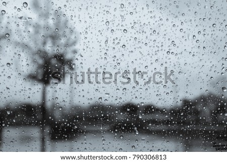 Dark and rainy day; raindrops on the windshield; tree shapes visible in the background; black and white