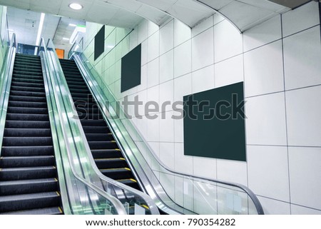 Public escalator with blank billboard on wall in subway