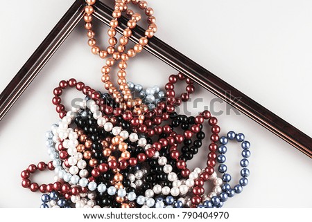 Pearl beads lined in a brown frame on a light background. Closeup, view from above. Different colors