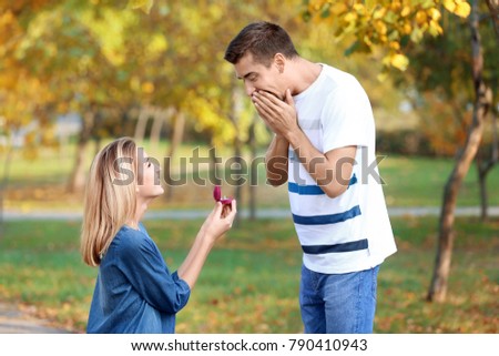 Young woman with engagement ring making proposal of marriage to her boyfriend in park Royalty-Free Stock Photo #790410943