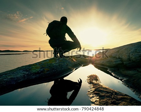 Lonely man hiker sits alone on the rocky  coast and  enjoying sunset. View over rocky cliff to free ocean