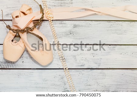 Ballet classic dancing shoes with pointed toe and hard metal insole lie on wooden theater stage background and diadem with rhinestones and pearl necklace. Ballet training concept. Top view.