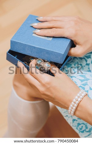Young adult white woman in fancy dress opening a gift box with decorative item. Valentine Day, birthday or another holiday present concept. Vertical close-up capture, selective focus.