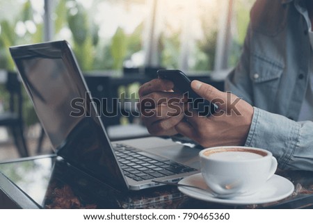 Casual business man working on laptop computer, browsing internet and using mobile smart phone with cup of coffee on table at coffee shop, working at cafe, anywhere office concept, close up