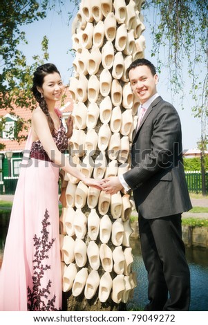 Romantic young asian couple in love standing in front of tree with wooden shoes.