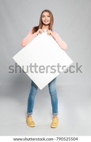 Young woman with blank advertising board on grey background