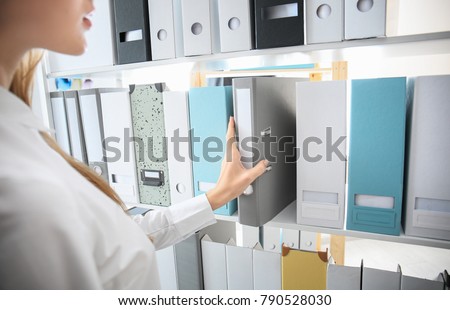Young woman taking folder with documents from shelf in archive Royalty-Free Stock Photo #790528030