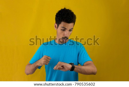 Worried man pointing to the watch on his wrist isolated in a yellow background. Concept image for social media and advertisements.