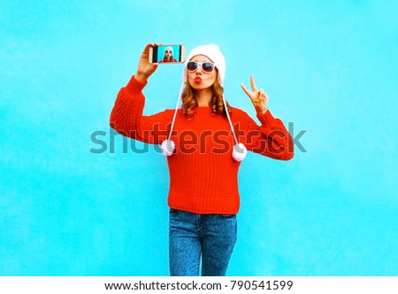 Pretty young woman takes a picture self portrait on a smartphone on blue background