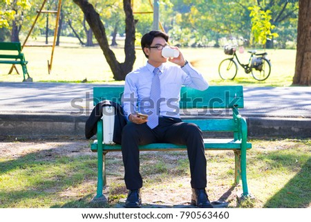 Businessman, He is sitting on bench in park. He is thinking about business. He is drinking coffee beside business bag. Photo concept  business and relax time.