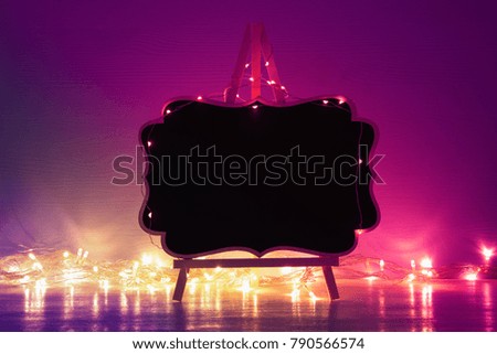 Image of empty blackboard with shny gold garland lights over wooden table