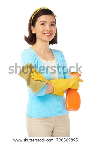 Portrait shot of pretty Asian housewife looking at camera with toothy smile while holding rag and spray cleaner in hands, isolated on white background