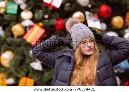 Attractive young red haired woman wearing winter outfit, posing on the background of Christmas spruce