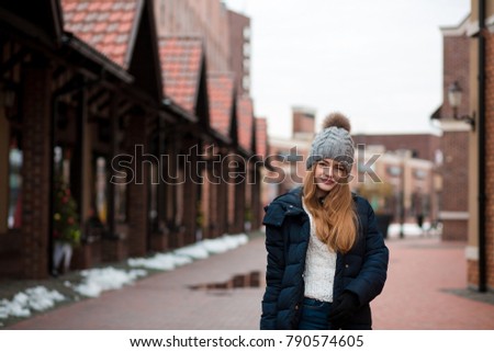 Cool young woman wearing black winter coat and knitted hat posing at the street in Kyiv