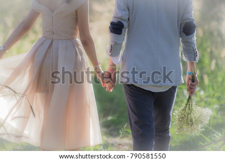 blurred photo of bride and groom hand in hand to take pictures before the wedding in the wild grass.