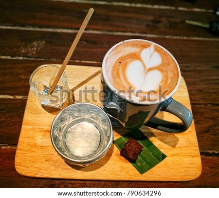 A cup of hot coffee with latte art and a piece of brownie on banana leaf