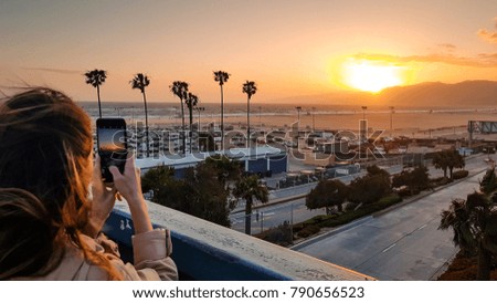 Girl taking a photo of sunset over the Santa Monica beach, Los Angeles, California, USA