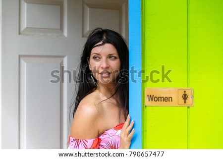 Thoughtful woman leaning against a restroom door of a bright green wooden hut on Oahu, Hawaii looking thoughtfully over her shoulder as she watches something in a close up view