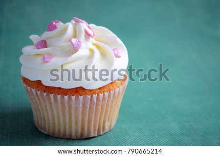 Cupcake for valentine's day with whipped cream and pink confectionery sprinkling In the form of hearts on blue background. Picture for a menu or a confectionery catalog.