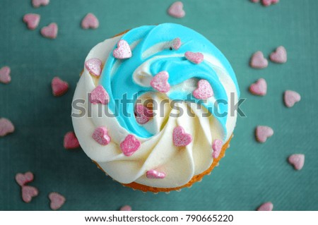 Cupcake for valentine's day with whipped cream and pink confectionery sprinkling In the form of hearts on blue background. Top view. Picture for a menu or a confectionery catalog.