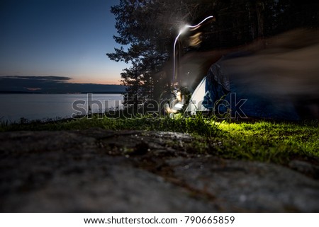 Long exposure of person pitching a tent at night on coastal area