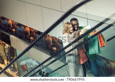 young couple taking selfie while riding escalator at shopping mall