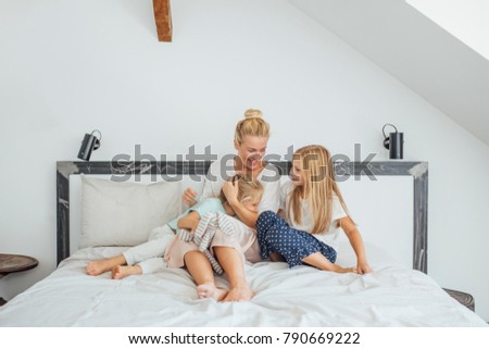 Pretty blonde Caucasian woman enjoying cuddling her daughters in bed.