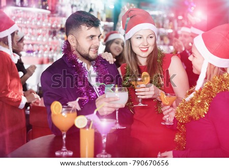 Young  man and two women with cocktails in Santa hats celebrating at nightclub