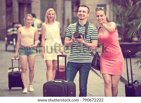 joyful young couple with luggage and camera taking pictures walking by street
