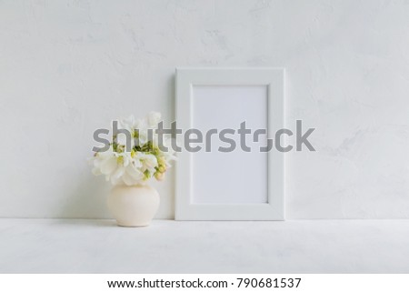 Mockup with a white frame and white spring flowers in a vase on a light background