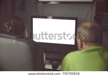 Two peoples is working on computer with blank monitor screen with copy space. A girl and a man are looking for information on the Internet. Blurred photo from back view.