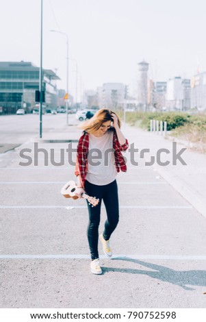 Young beautiful woman walking in the city holding ukulele - busker, city living, music concept