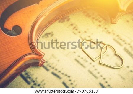 Valentine's day / eternal love or special occasion concept : Two / twin hearts near a stradivarius type violin on blurred musical notes in a romantic love song sheet music. Vintage sepia tone color.
