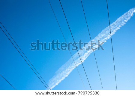 Clear blue sky, wires and cables with electricity, tracks and traces of white cloud made by airplane. Simple and abstract lines and lanes.