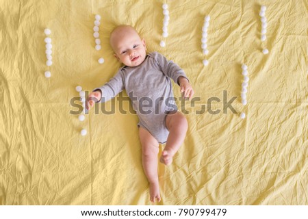 top view of funny infant child lying surrounded with exclamation marks made of cotton balls in bed 