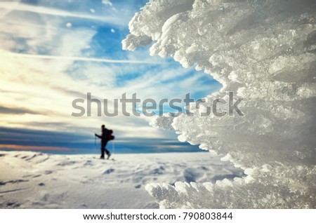 Close up picture of ice formations at sunset, cross-country skier silhouette in distance, selective focus.