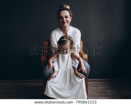 Young beautiful mother plays with her 3 year old daughter on a dark background.