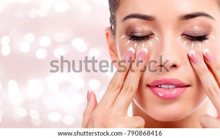Pretty woman massaging her face, skin treatment antiaging concept. Abstract background with blurred lights