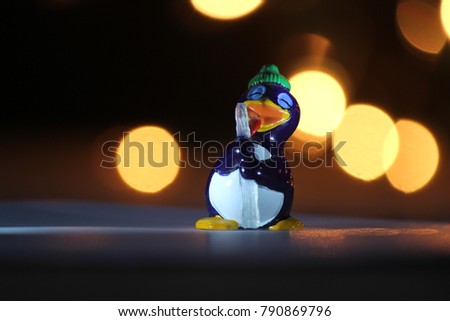 a funny pingo animal figurine toy is licking with its tongue at an icicle with bokeh in the background