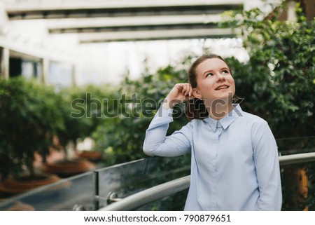 Office place with girl stand near plants. Smiling girl look at camera and around with pretty face. Office worker break, plants around.