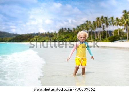 Child on beautiful beach. Little boy with toy boat running and jumping at sea shore. Ocean vacation with kid. Children play on summer beach. Water fun. Kids swim. Family holiday on tropical island.