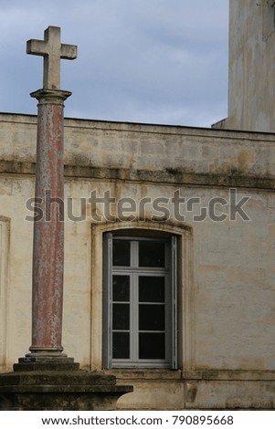 View of a stone cross place on a high column in front of a house. Symbol of the faith in god. A peaceful picture with a blue sky. A tall religious monument in the city of Montpellier France.