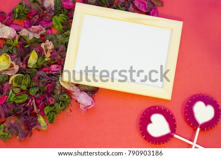 The concept of St.Valentine's Day with a blank wooden photo frame and rose petals and leaves, red background top view, copy space