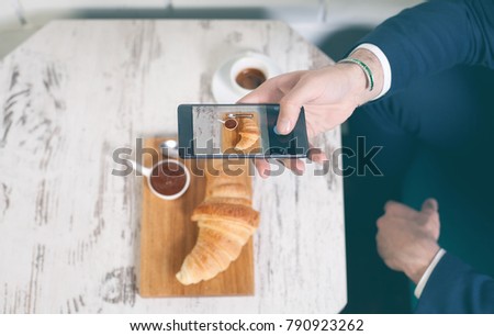 Taking a picture of breakfast with croissant, coffee and chocolate