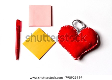The red fabric heart on the right and 2 square post it notes with red pen in the left and all are on the white background.  Concept Valentine's day and Love notes.