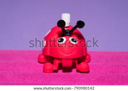 Wind-up red Valentine love bug with white polka dot hearts stands on a pink leather floor against a purple background. 