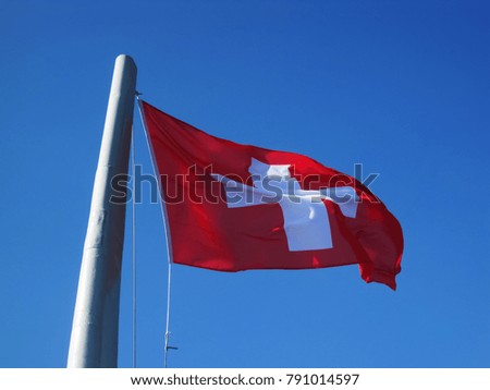 Nacional red Swiss flag with white cross under the blue sky on the wind                              