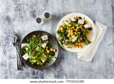 two plates of vegetable salad with chickpeas, arugula, feta cheese or tofu and black olives on a natural stone background. healthy eating Royalty-Free Stock Photo #791016580
